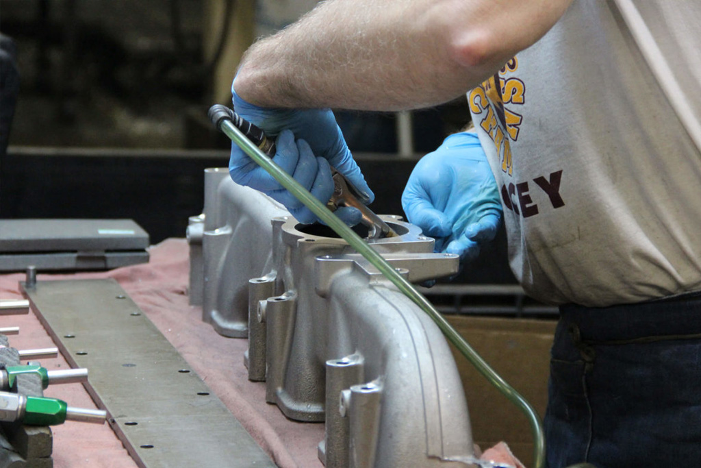 At a work table, a Dee Manufacturing machinist uses a hand tool to smooth the surface interior of a metal casting.