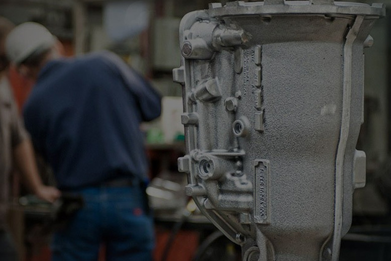 Cast aluminum part in the right foreground, with an ATEK Metal Technologies employee at work, facing away, at a table in the background.