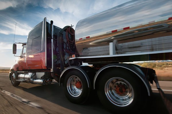 Close side view of semi-truck hauling a tanker, with an agricultural landscape reflected in the tanker.