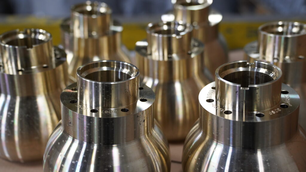 Seven uniform, smooth-finish brass and bronze components set on table at Wisconsin Aluminum Foundry.
