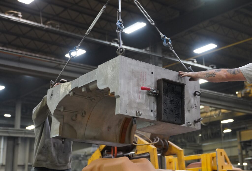 Wisconsin Aluminum Foundry workers guide a large metal casting harnessed to a lift across the facility.