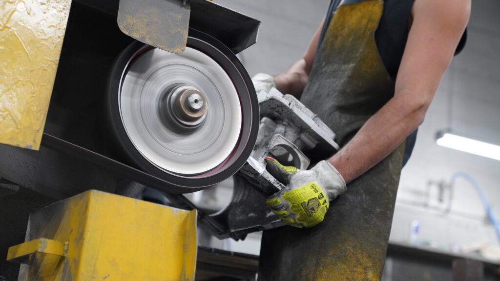 Wisconsin Aluminum Foundry worker operate a large sander to smooth off excess aluminum on a casting.