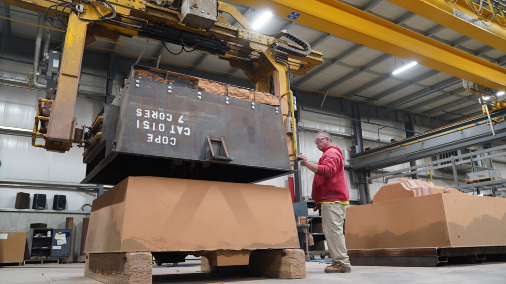 A Wisconsin Aluminum Foundry worker operates an air set sand molding machine to produce a mold for a heavy duty part.