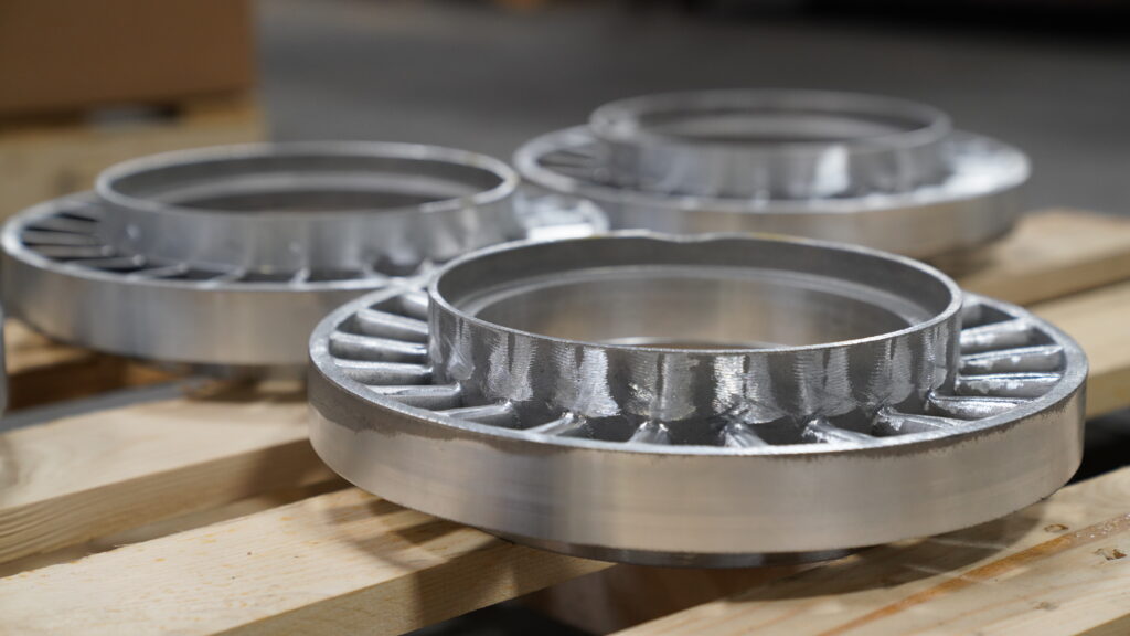 Closeup of three Wisconsin Aluminum Foundry cast metal parts sitting on a wood pallet to cool.