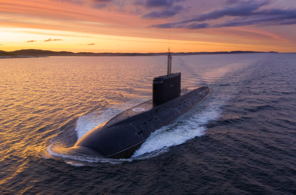 Under a sunset, a submarine emerges from the ocean.