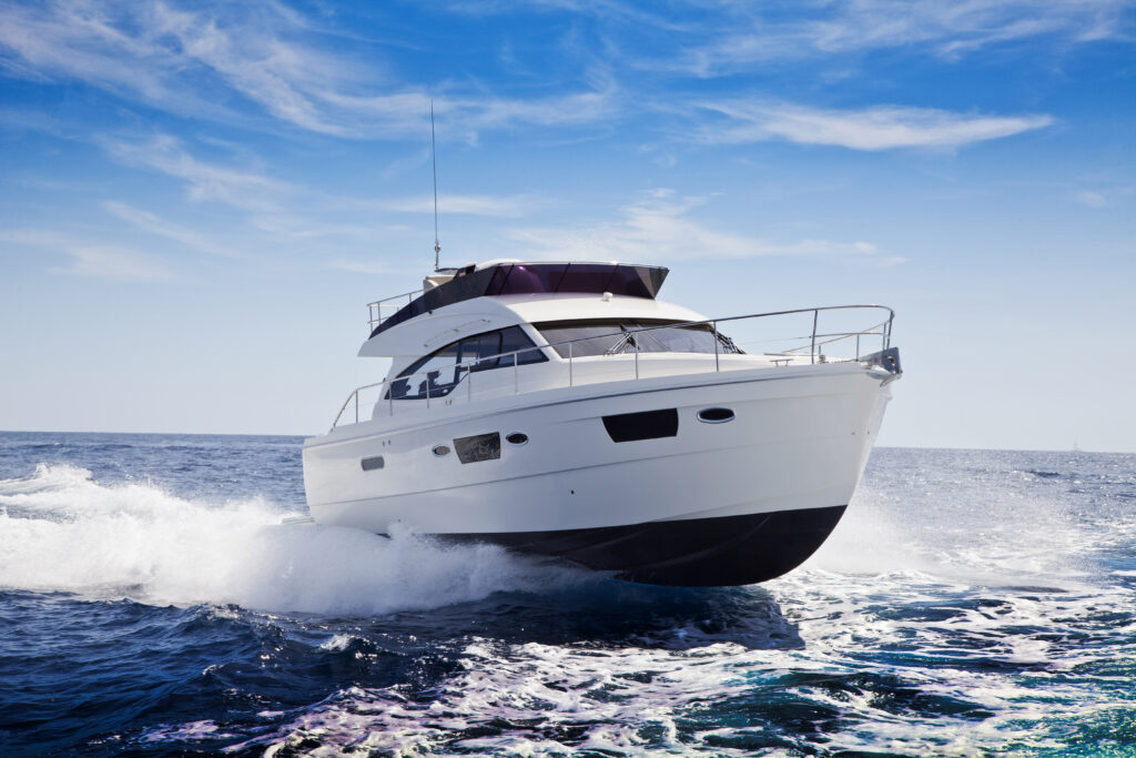 Small yacht with enclosed cabin, front railing jets across open blue water, with a sky of hazy clouds above.