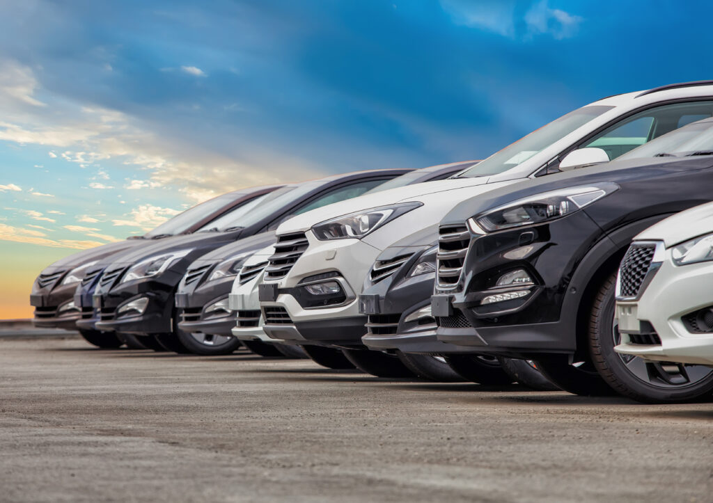 Nine new cars and SUVs are lined at an angle beneath a sky tipping toward sunset.